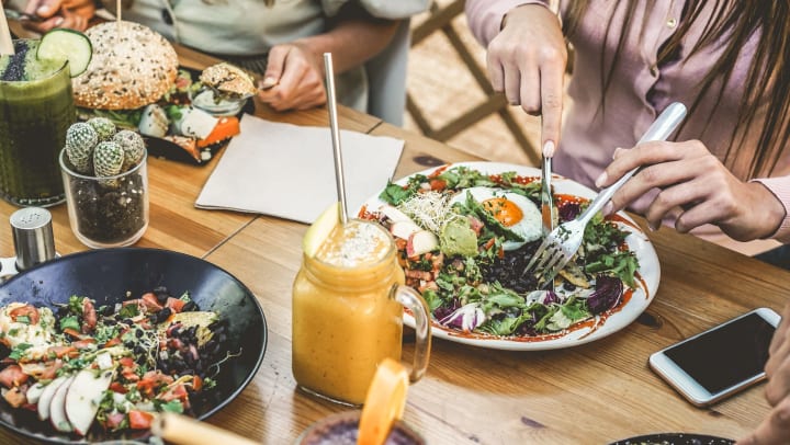  Disembodied hands cutting their meal on a table full of foods and orange drinks in mason jars. 