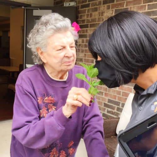 Smiling sharing a flower with caretaker at Oxford Glen Memory Care at Grand Prairie in Grand Prairie, Texas