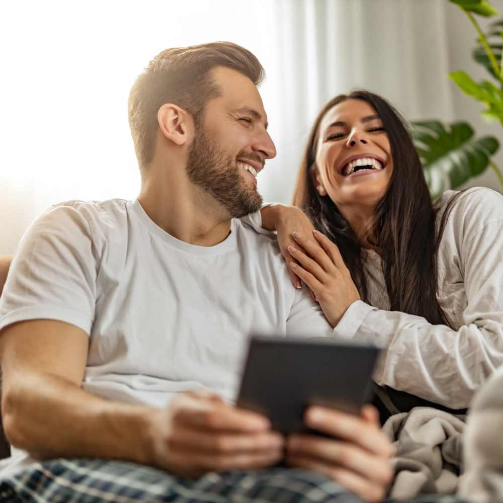Resident couple smiling while seating on the couch at Fox Crossing Apartments in Burlington, Wisconsin