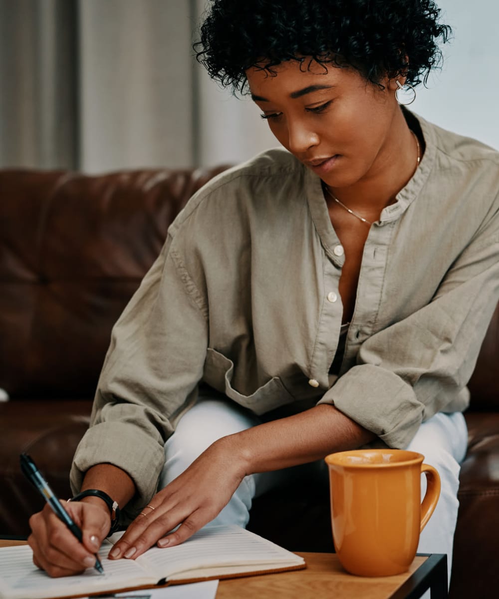 Woman writing at her coffee table while enjoying a cup of coffee at Big Sky Flats Apartments in Washington, District of Columbia