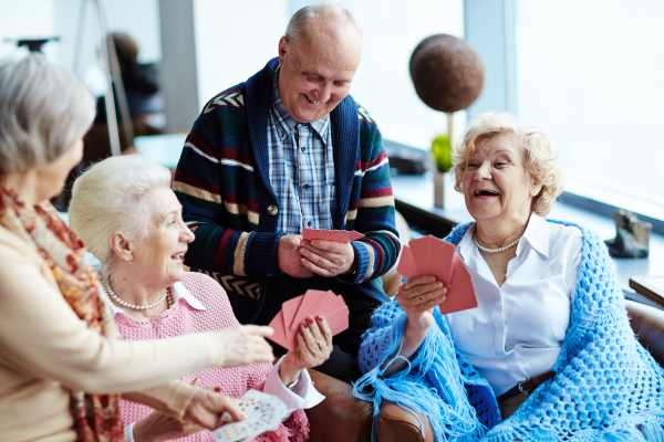 Group of senior residents laughing and enjoying a card game together in a bright, cheerful community space.