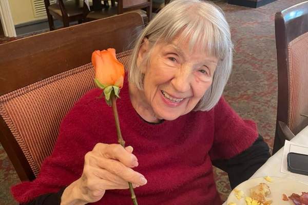 Beautiful elderly woman smiling and holding cut rose and stem for Mothers Day