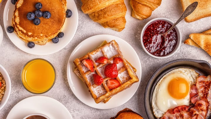 Aerial view of a collection of breakfast/brunch food on a table with a white table cloth.