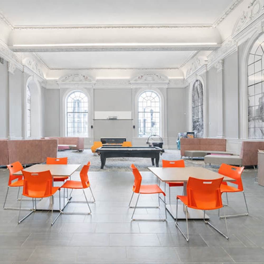 Bright community lounge with orange chairs, pool table, and large windows highlighting a spacious, open layout at Flats on Fifth in Louisville, Kentucky