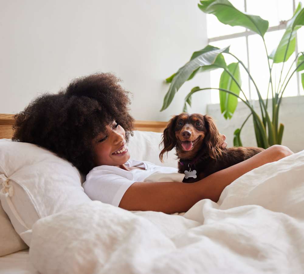 Woman smiling with dog in bed at Avia Lofts at Maple Road in Amherst, New York 