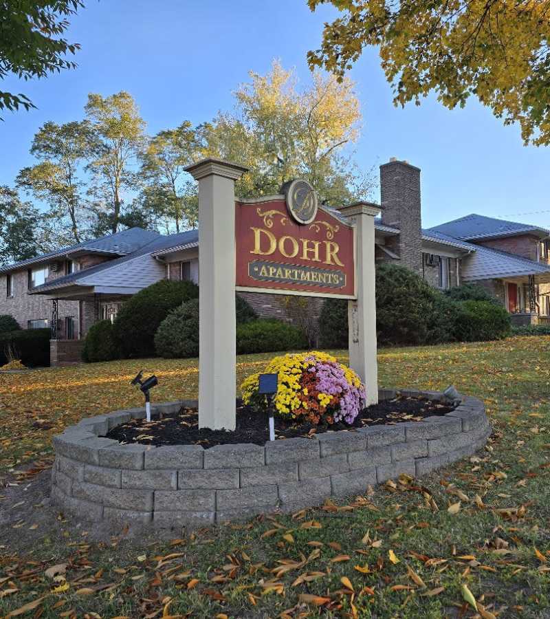 Dohr Apartments sign surrounded by colorful flowers and landscaped greenery on a sunny day at Dohr Apartments in Rochester, New York