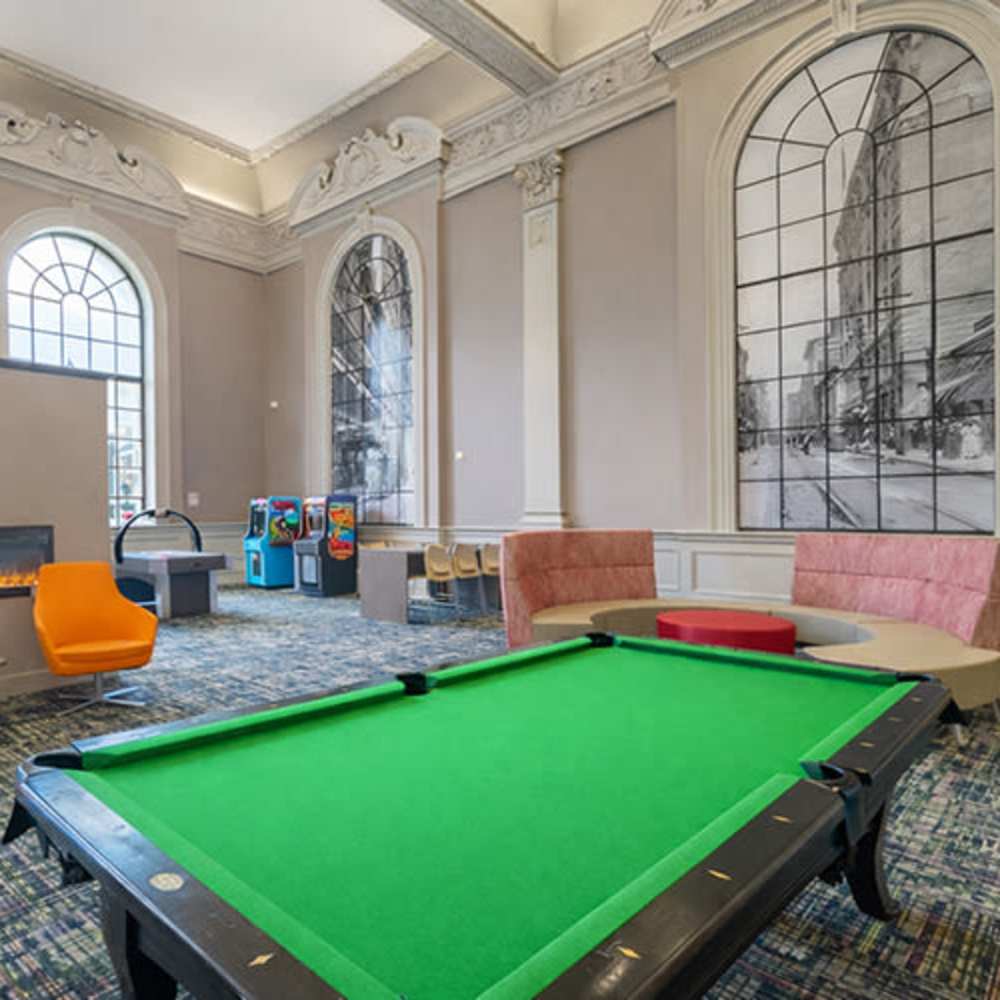Bright game room featuring a green pool table, arcade games, and modern seating arrangements at Flats on Fifth in Louisville, Kentucky