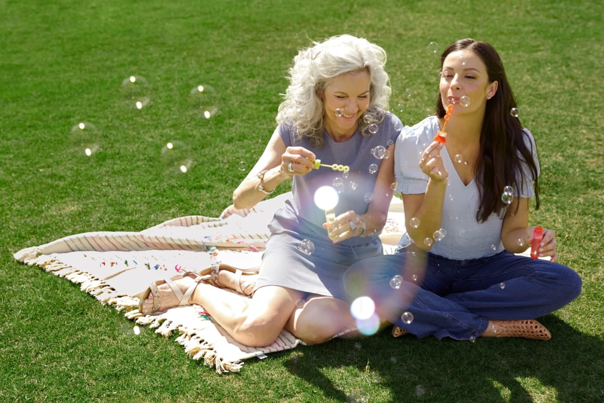 Two friends sitting at a park blowing bubbles at BB Living Light Farms in Celina, Texas