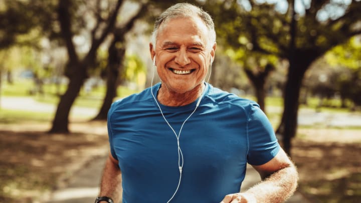 An elderly man running through a park, surrounded by trees and grass, showcasing an active lifestyle.