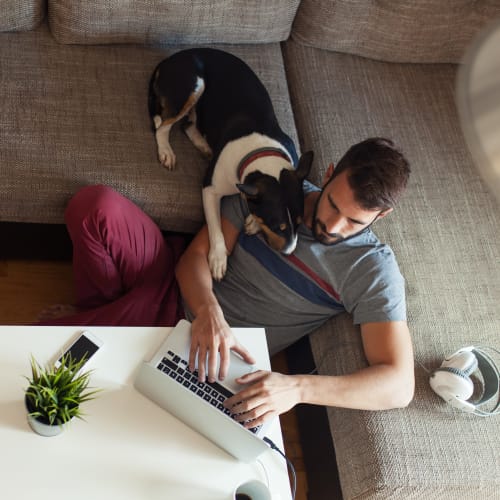 A resident relaxing with a dog and using a computer in a home at Osprey Point in Virginia Beach, Virginia