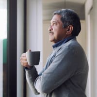 An older resident holding a mug and looking out a window at Retreat at the Park in Burlington, North Carolina