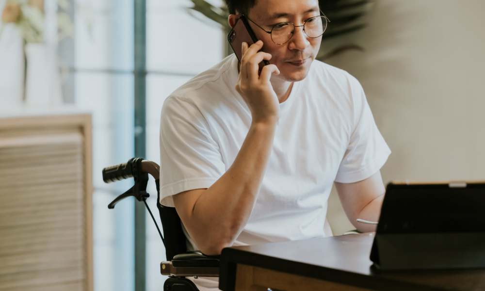 Man in wheelchair talking on phone at desk with tablet and modern decor at Spring Valley Apartments in Lexington Park, Maryland
