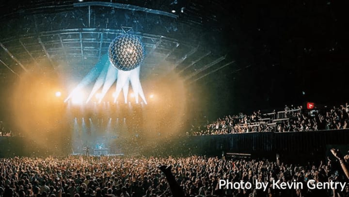 Image of a crowd of people at a concert with a large disco ball centered over the stage