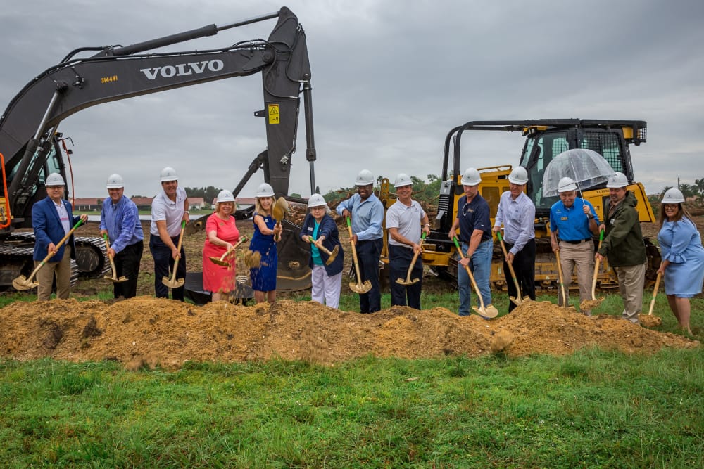 Groundbreaking shovel photo with city leaders and development team with tractors in the background
