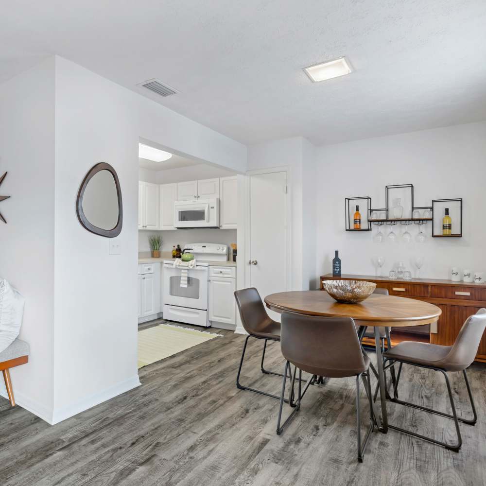 Bright open layout featuring wood-style flooring, modern kitchen with white cabinetry and stainless steel appliances, dining area with round table at Carlton Arms North in Tampa, Florida
