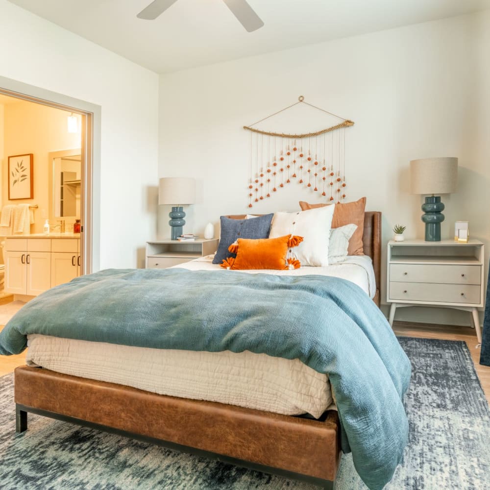 A well-made bed by a large window in an apartment bedroom at Cypress McKinney Falls in Austin, Texas