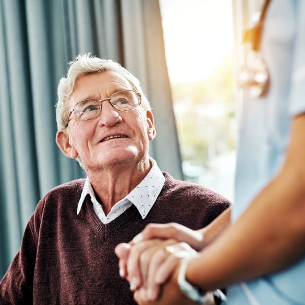 Resident holding hands and looking to a caretaker at a Living Care Lifestyles community