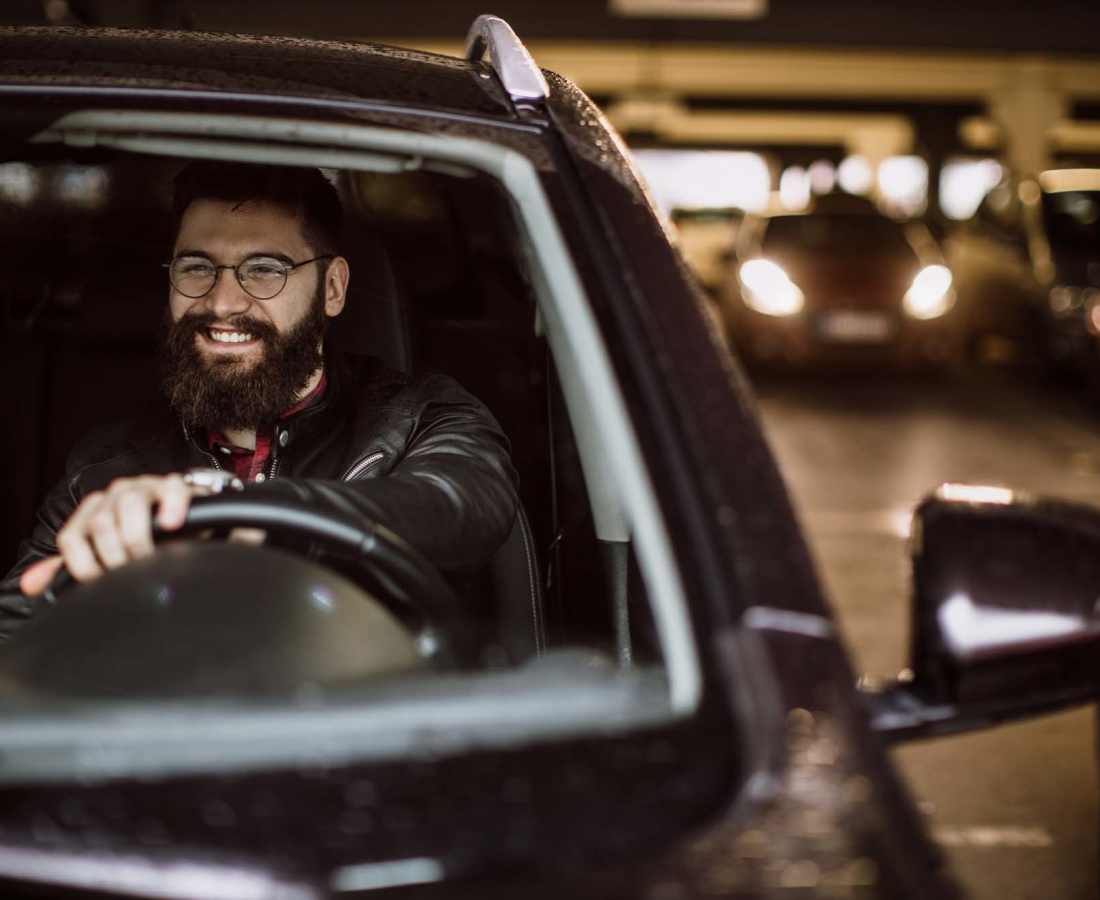 Smiling man with beard driving a car in a parking garage at Valley Brook Townhomes in Rochester, New York