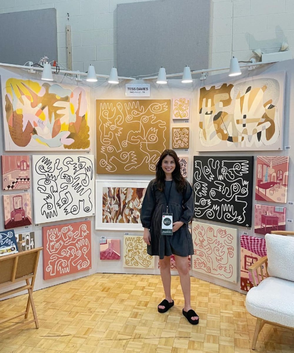 Artisti Tess Davies standing in front of a display of a variety of her artwork.