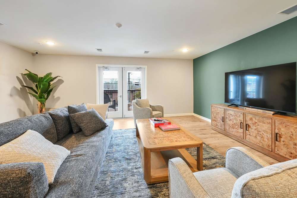 Modern living room with gray sofas, wooden coffee table, large TV, and natural light from patio doors at Hawkins Pointe in Hendersonville, North Carolina