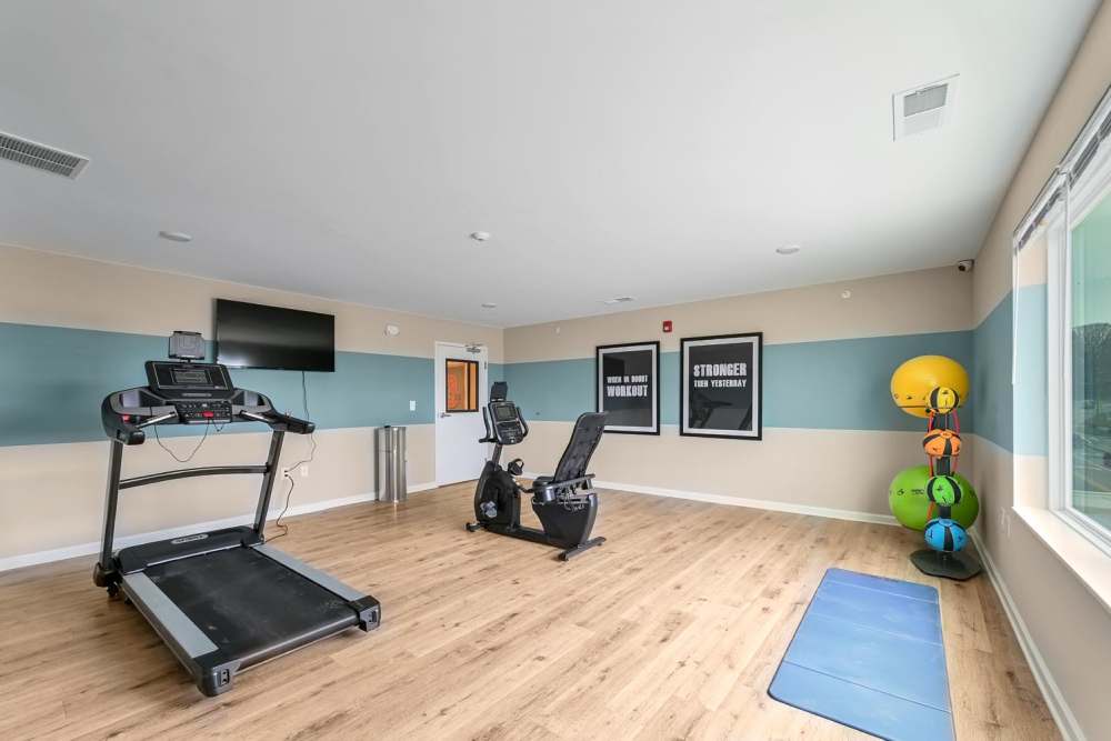 Modern fitness room with treadmill, stationary bike, wood-style flooring, and motivational wall art at Hawkins Pointe in Hendersonville, North Carolina