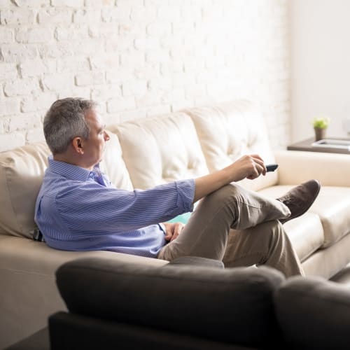 A resident setting on the couch and holding a television remote control at Seaside Village in Oceanside, California