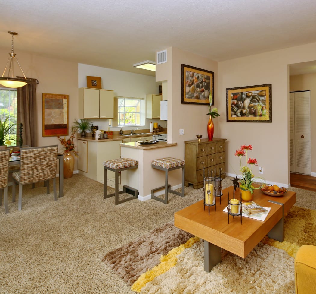 Model home living room with plush carpet looking into kitchen and dining area at IMT Pinebrook Pointe in Margate, FL