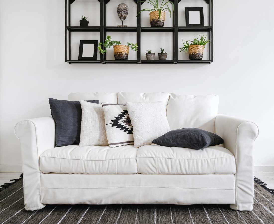 White sofa with decorative pillows on a patterned rug against a minimalist wall shelf with plants at Dohr Apartments in Rochester, New York