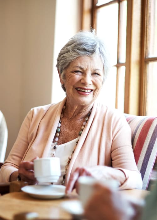 Smiling old woman sitting on a chair with her tea at The Pillars of Grand Rapids in Grand Rapids, Minnesota