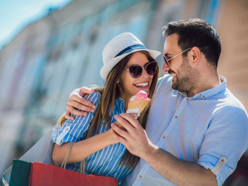 Couple enjoying ice cream while smiling and embracing outdoors with shopping bags nearby at 43 North Apartments in Grand Haven, Michigan
