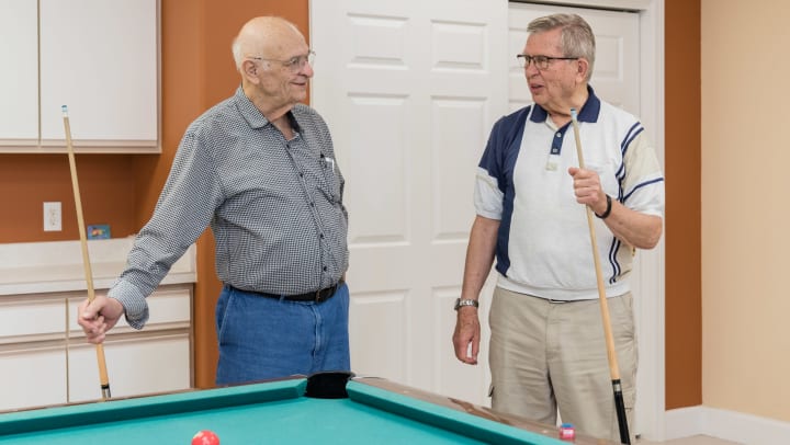 Image of two male Touchmark residents playing pool in the billiards room.