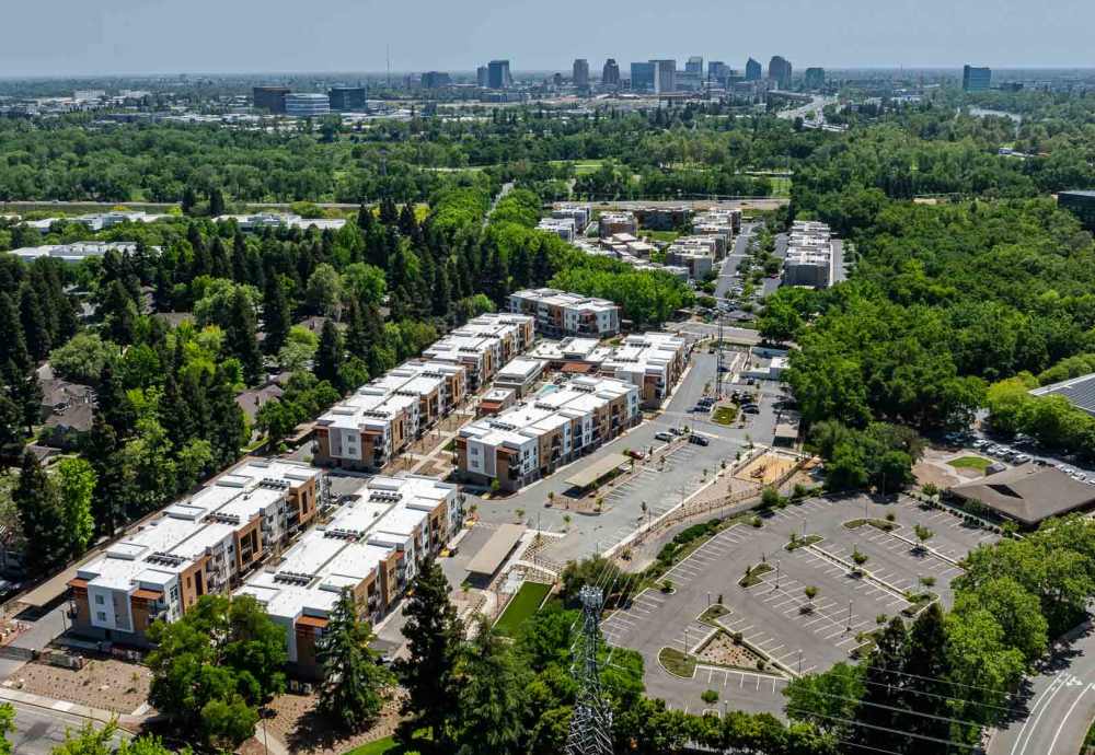 Aerial view of residential complex surrounded by greenery and city skyline at Sutter Green Apartments in Sacramento, California.