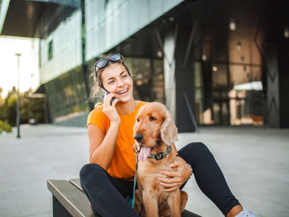Woman sitting with dog, talking on phone near Cape At Savona Apartments in Cape Coral, Florida