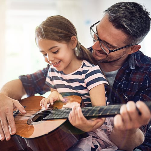 A father teaching his daughter to play guitar in a home at Eagleview in Joint Base Lewis McChord, Washington