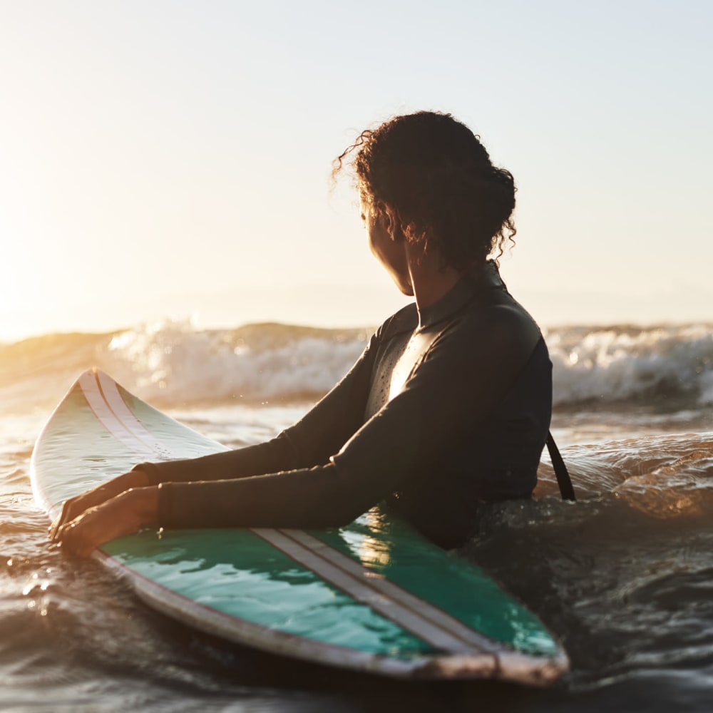 A woman in the ocean with a surf board near Dolphin Marina Apartments in Marina Del Rey, California