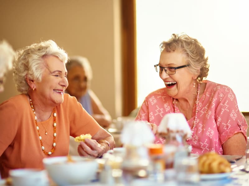 Two residents laughing at the dining table at Shawnee Memory Care in Shawnee, Oklahoma. 