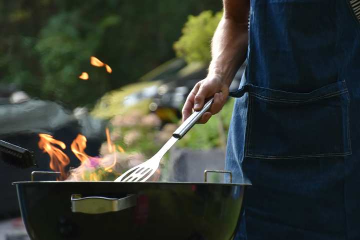 Close up photo of a person grilling food with a spatula over a round charcoal grill