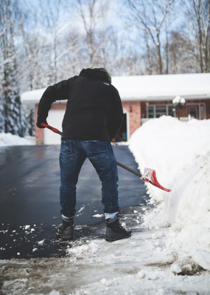 A photo of someone from behind shoveling snow from a driveway