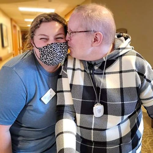 Masked caretaker talking to a seated resident at The Oxford Grand Assisted Living & Memory Care in Wichita, Kansas