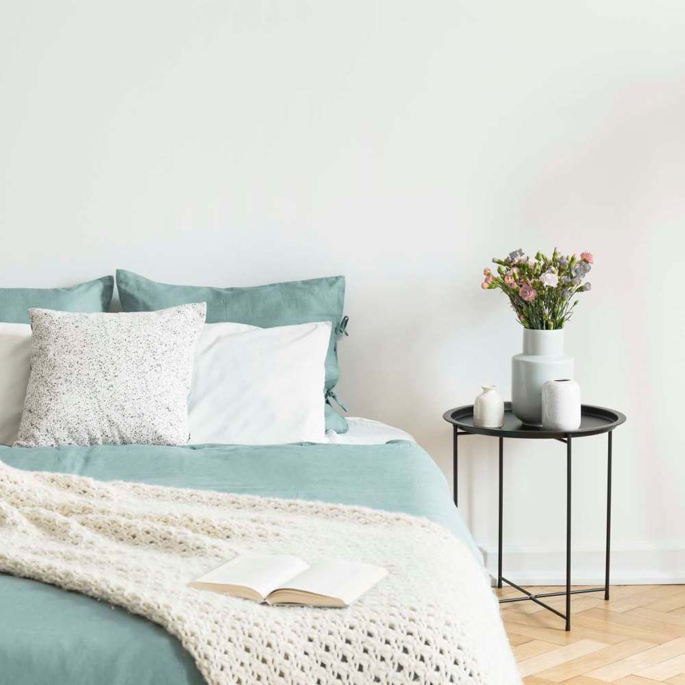 Modern bedroom with large bed and side table with vase at Grayling Pines Apartments in Grayling, Michigan