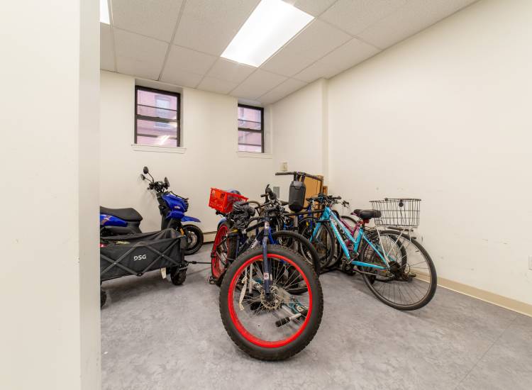 Bicycle storage area with various bikes and a cart in a well-lit room at 15-25 Hemenway Apartments in Boston, Massachusetts