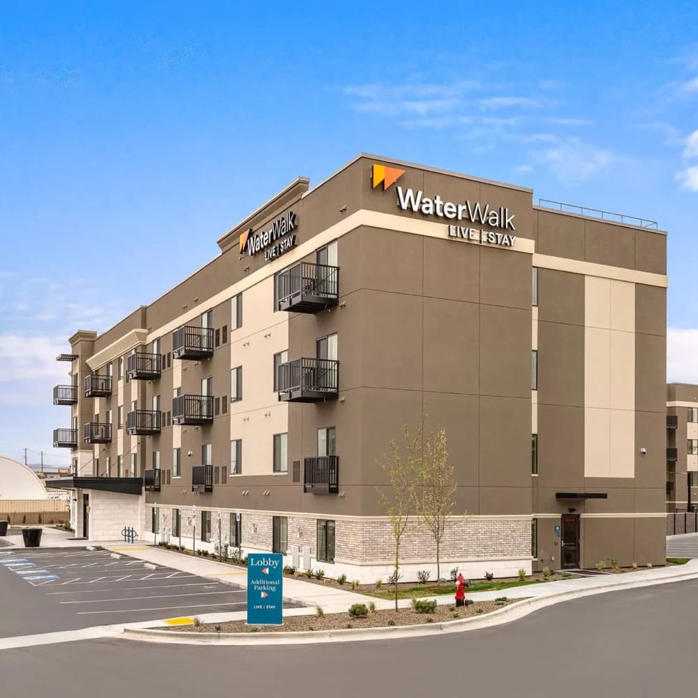 Modern apartment community with balconies, landscaped entrance, and clear blue sky at WaterWalk Boise - Meridian in Meridian, Idaho