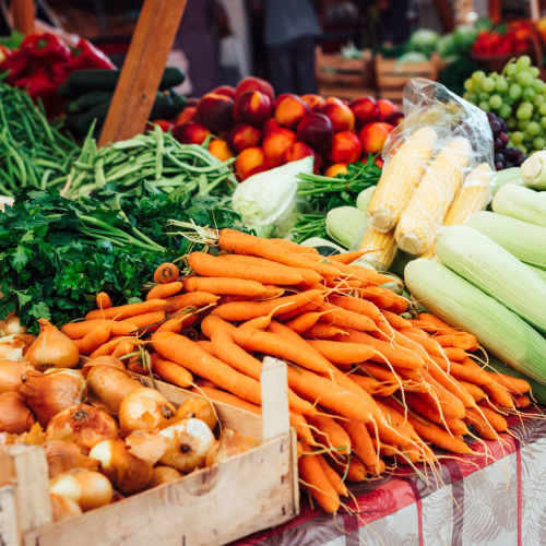 Vibrant display of fresh vegetables including carrots, corn, and greens at a market stall near Arlington Greene in London, Kentucky