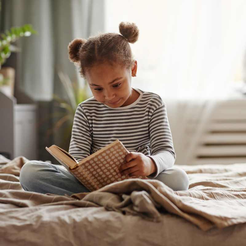 A young girl reads a book on her bed at Commons on Potomac Square, Sterling, Virginia