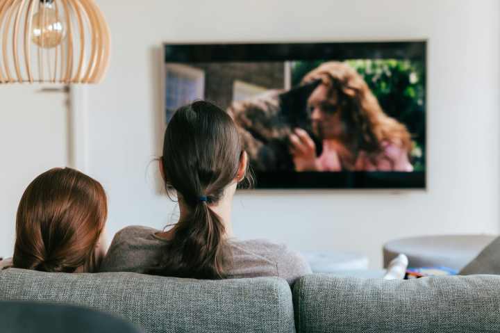 behind the head photo of a mother and daughter sitting on a couch watching a movie on television