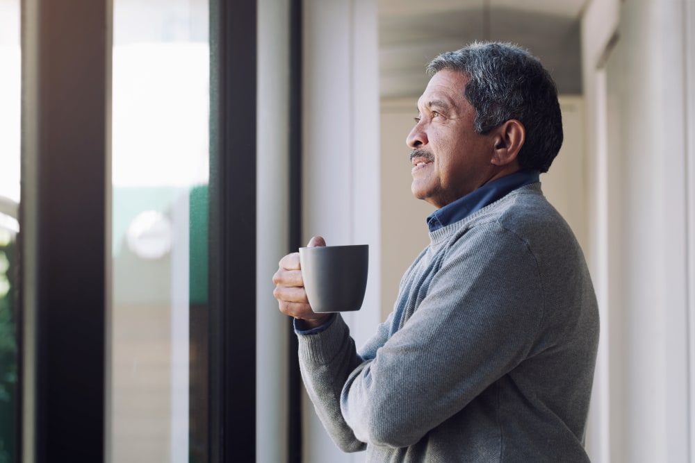 A man looking out a window holding a cup of coffee at Village at Glenhaven in Greenwood, South Carolina
