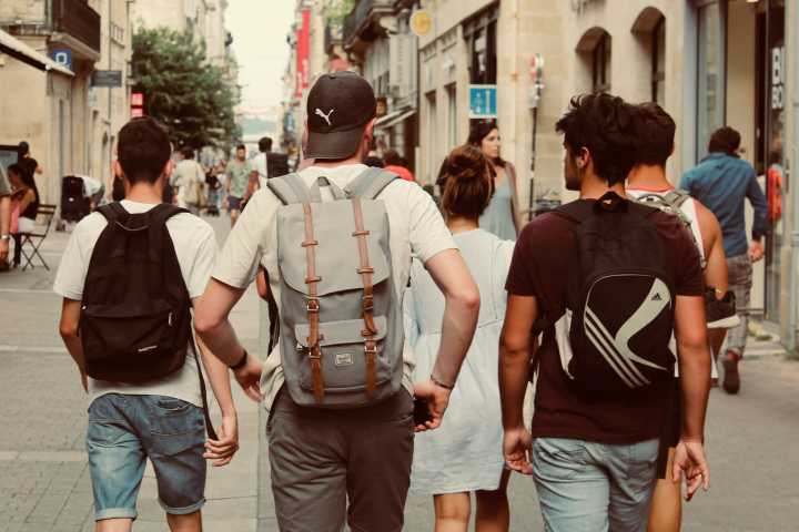 students walking through a pedestrian street with their backs to the camera with backpacks on 