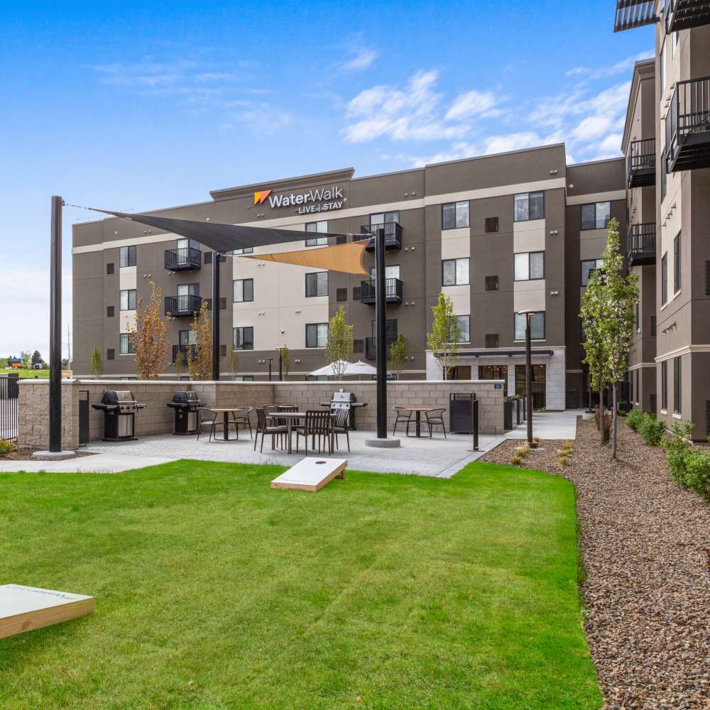 Outdoor grilling area with seating, landscaped lawn, and modern apartment buildings in the background at WaterWalk Boise - Meridian in Meridian, Idaho