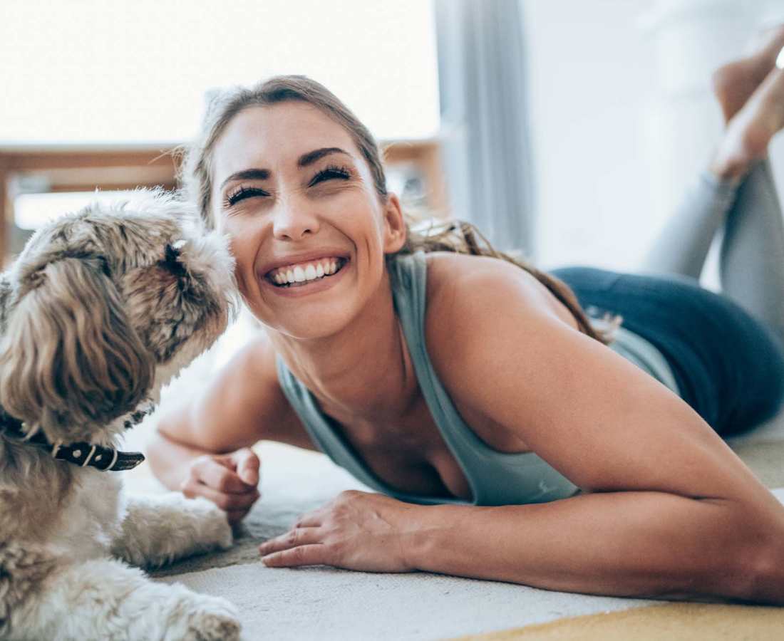 Woman smiling while lying on floor with playful dog, enjoying a pet-friendly atmosphere at Dohr Apartments in Rochester, New York