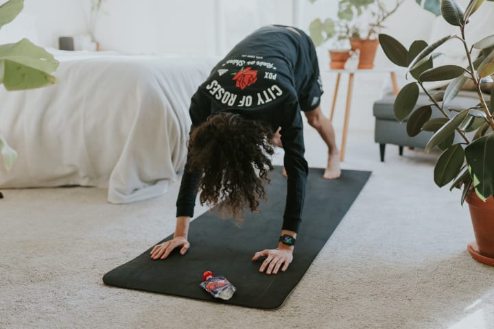 A person stretching in a downward dog yoga pose on a yoga mat in a bedroom. 